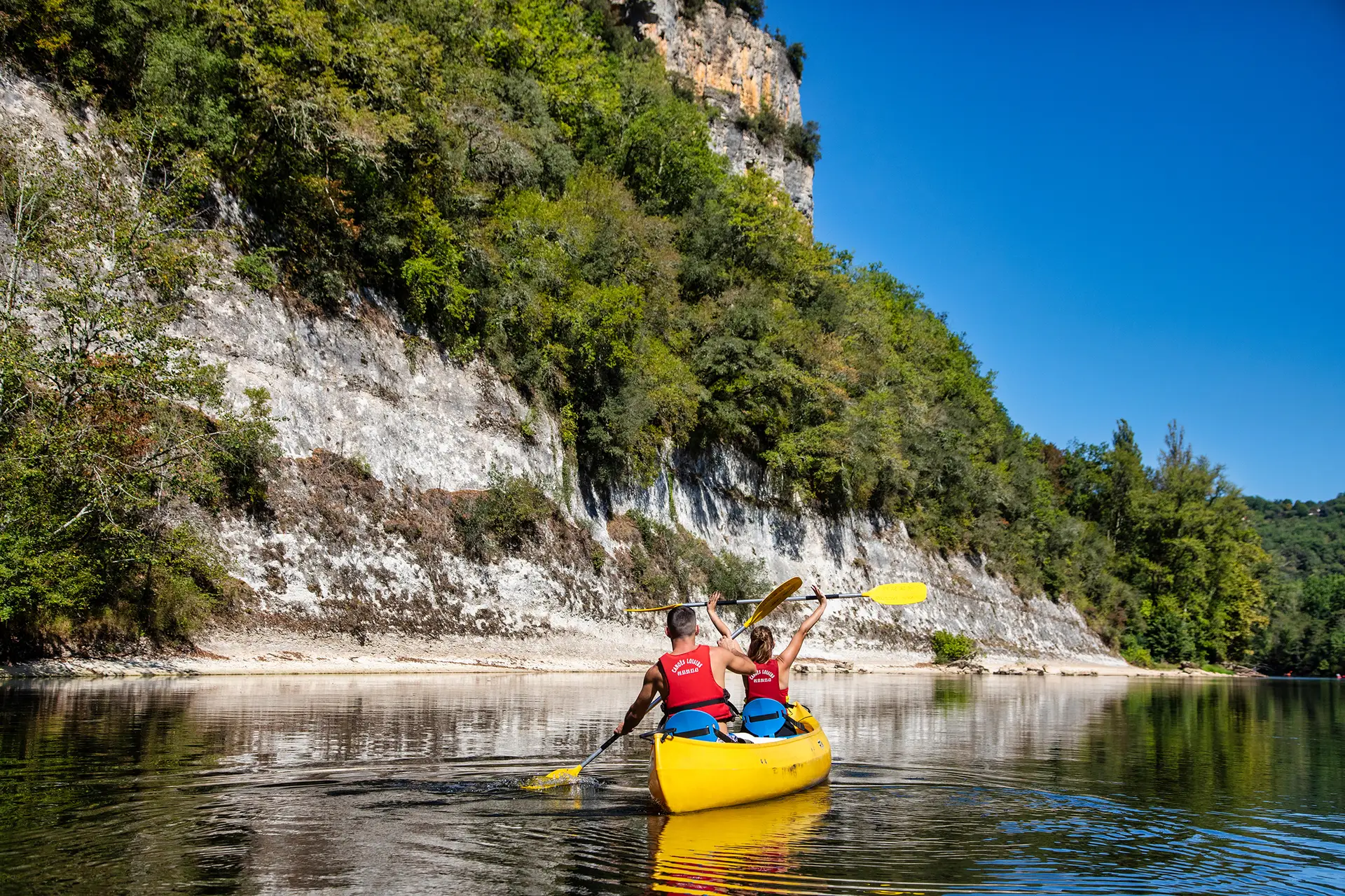 Couple heureux dans canoë sur la dordogne devant falaise blanche