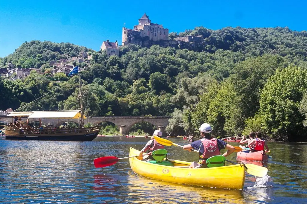 Canoë qui navigue sur la Dordogne qui croise une gabarre devant le chateau de Castelnaud-la-Chapelle